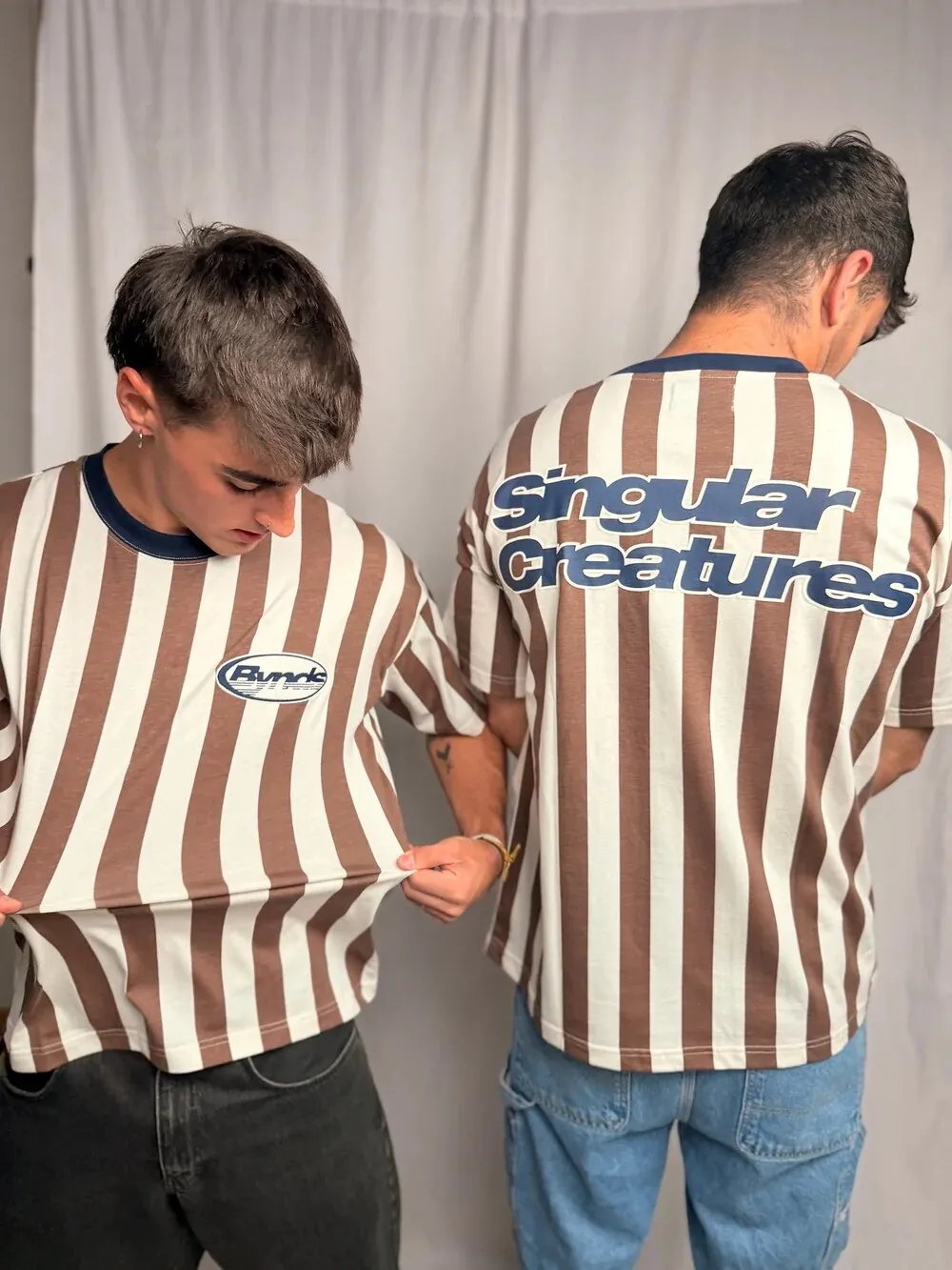 Two models in brown and cream striped BYNDS polo shirts with “Singular Creatures” on the back