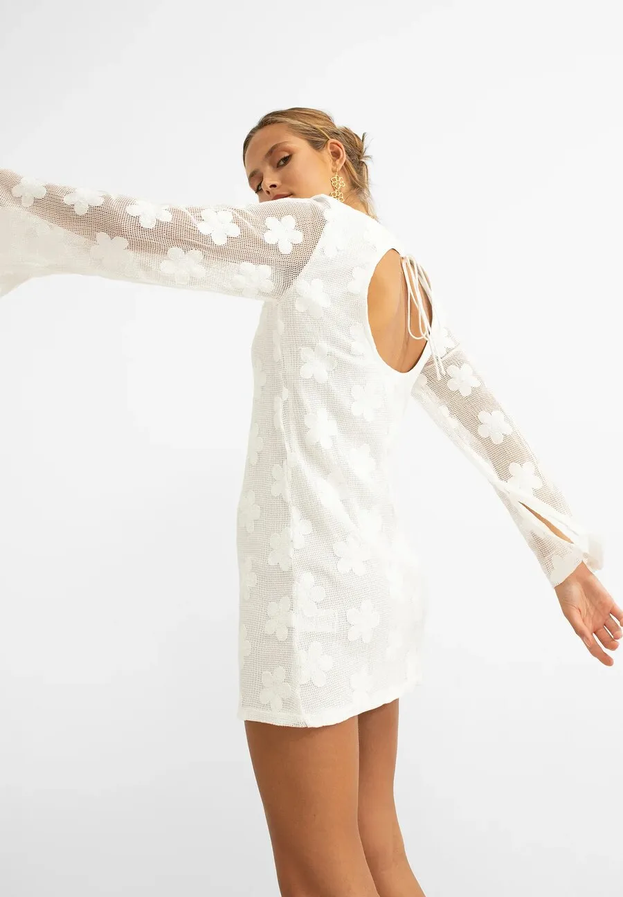 Woman in a short white dress with sheer flower-patterned sleeves and an open back, for Noon