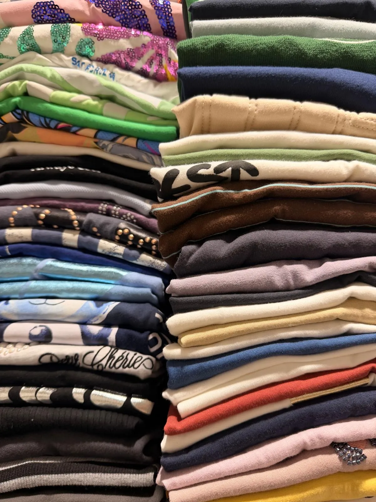 Stacks of folded tops in greens, blues, black and pastels, some with sequins and studs