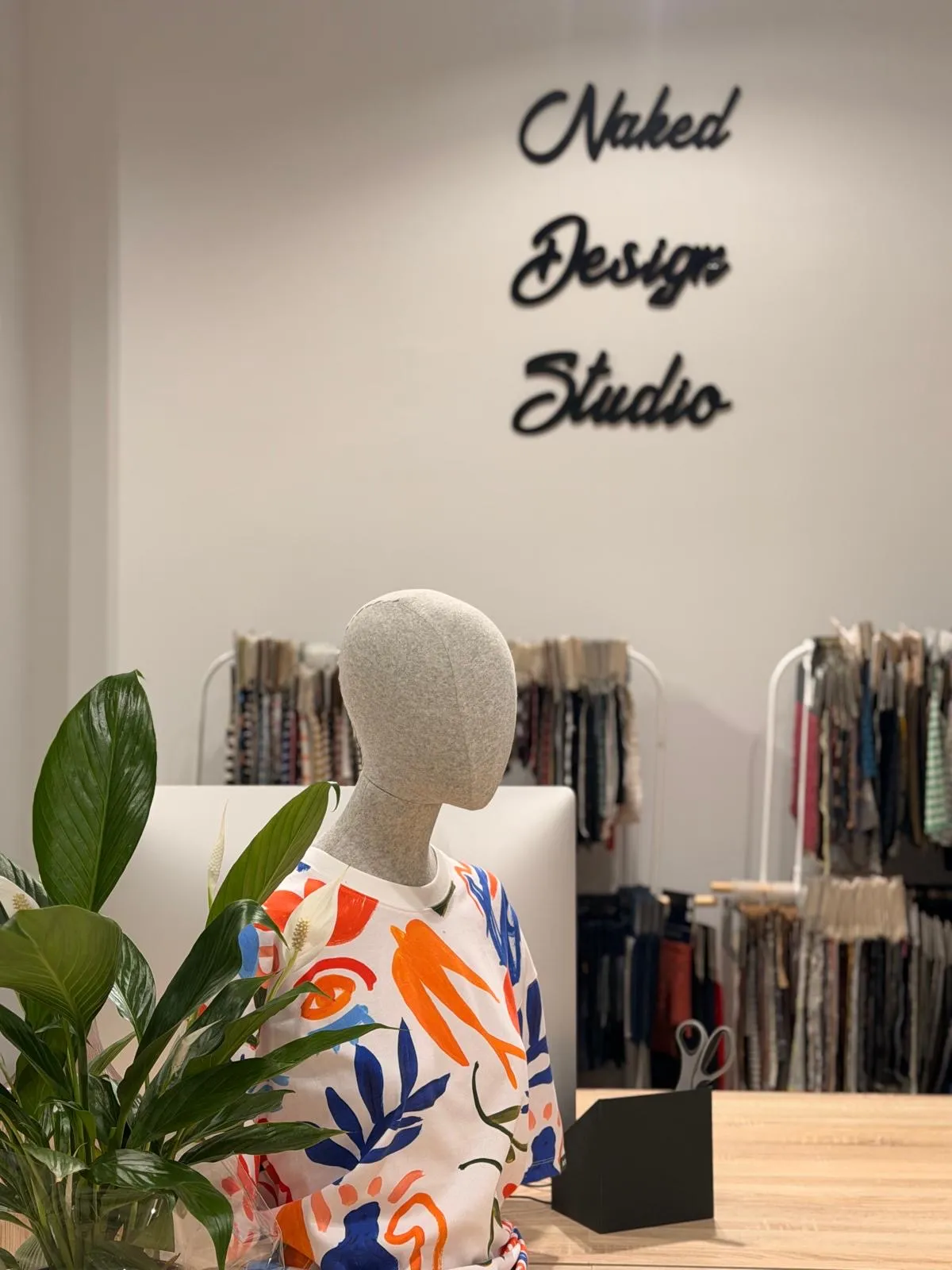 The Naked Design Studio sign on the wall, with a mannequin wearing a hand-painted print sweatshirt, a plant and fabric swatches behind